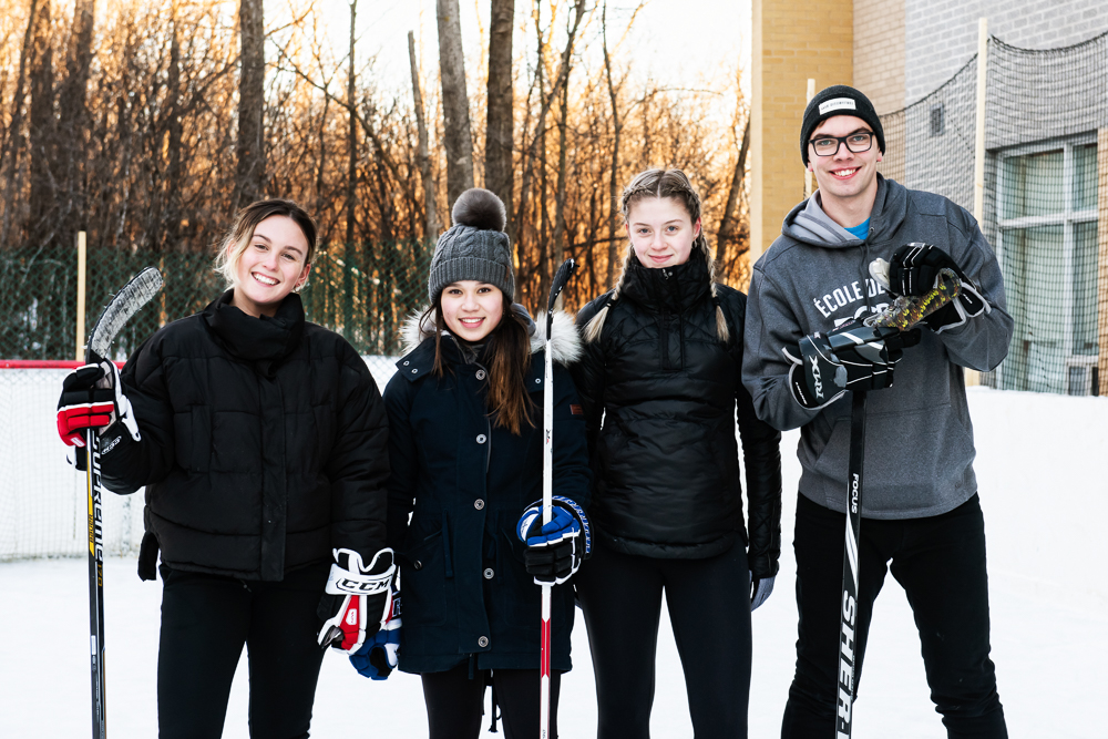 Quatre étudiants jouent au hockey sur la patinoire à l'arrière de la Résidence